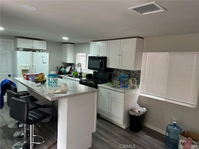 kitchen featuring black appliances, a kitchen island, dark hardwood / wood-style flooring, white cabinetry, and a breakfast bar area