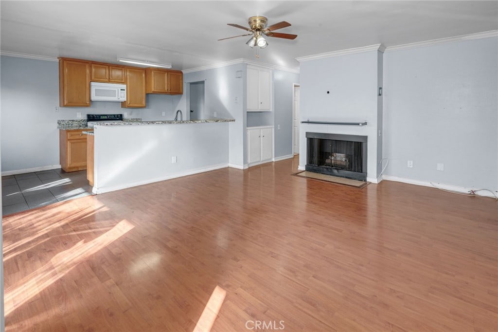 unfurnished living room with ceiling fan, wood-type flooring, sink, and crown molding