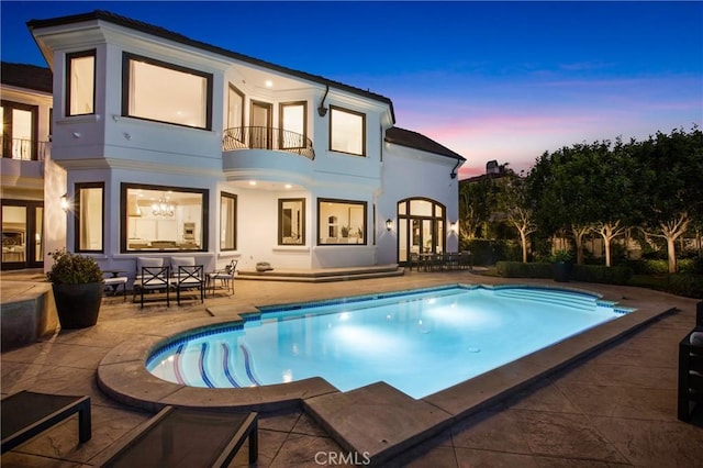 1 Moss Lndg, Laguna Niguel, CA 92677 - back of property at dusk featuring a balcony, a patio area, stucco siding, and an outdoor pool