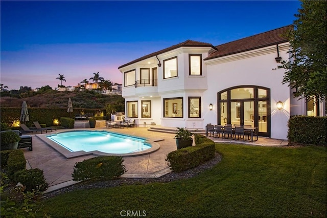 back house at dusk with a fenced in pool, a patio area, a balcony, and a lawn