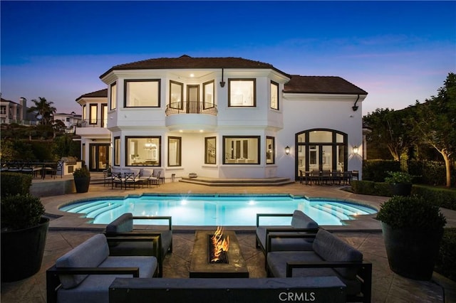 back house at dusk featuring french doors, a patio area, a balcony, and a fire pit