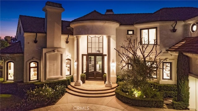 1 Moss Lndg, Laguna Niguel, CA 92677 - exterior entry at dusk with french doors, a chimney, and stucco siding