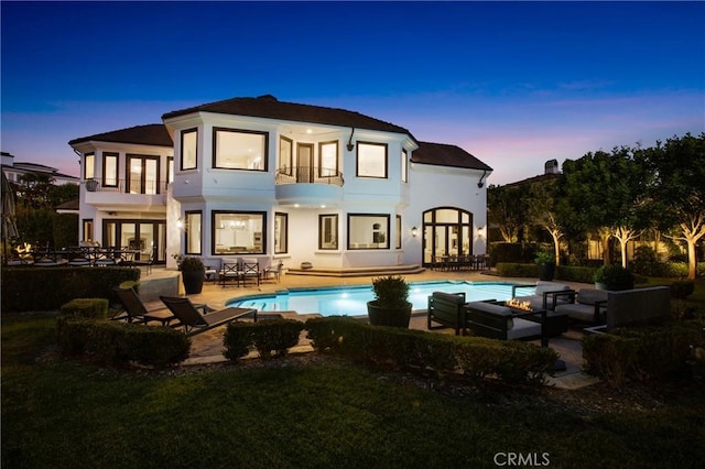 back house at dusk with a patio area and an outdoor living space with a fire pit