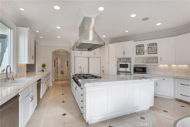 1 Moss Lndg, Laguna Niguel, CA 92677 - kitchen featuring appliances with stainless steel finishes, island range hood, arched walkways, backsplash, and a spacious island