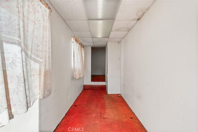 hall featuring dark colored carpet and a paneled ceiling