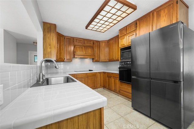 kitchen featuring decorative backsplash, kitchen peninsula, sink, black appliances, and tile counters