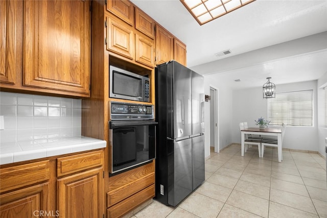 kitchen with tile countertops, black appliances, decorative backsplash, light tile patterned floors, and a notable chandelier