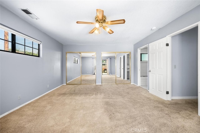 unfurnished bedroom with multiple closets, ceiling fan, and light colored carpet