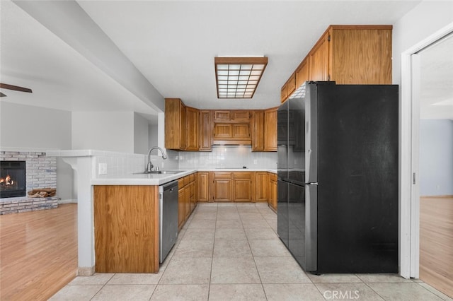 kitchen with black refrigerator, kitchen peninsula, stainless steel dishwasher, sink, and light hardwood / wood-style flooring