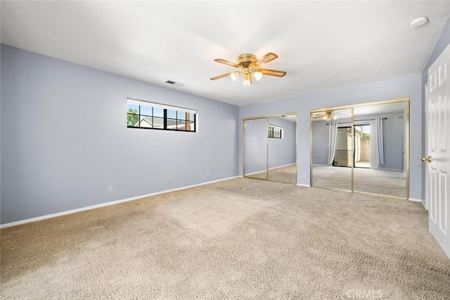 unfurnished bedroom with two closets, multiple windows, light colored carpet, and ceiling fan