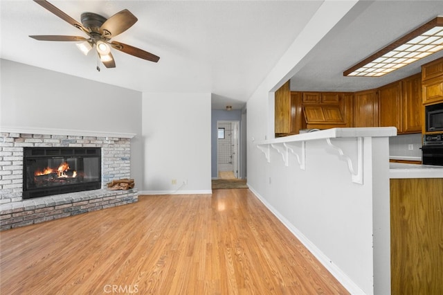 unfurnished living room with ceiling fan, a fireplace, and light hardwood / wood-style floors