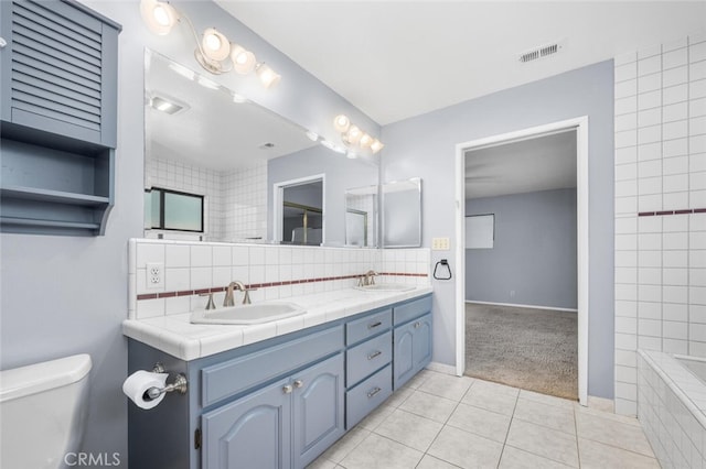 bathroom featuring tile patterned flooring, a relaxing tiled tub, toilet, decorative backsplash, and vanity