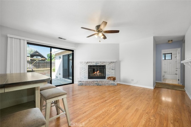 living room with ceiling fan, light hardwood / wood-style floors, and a brick fireplace