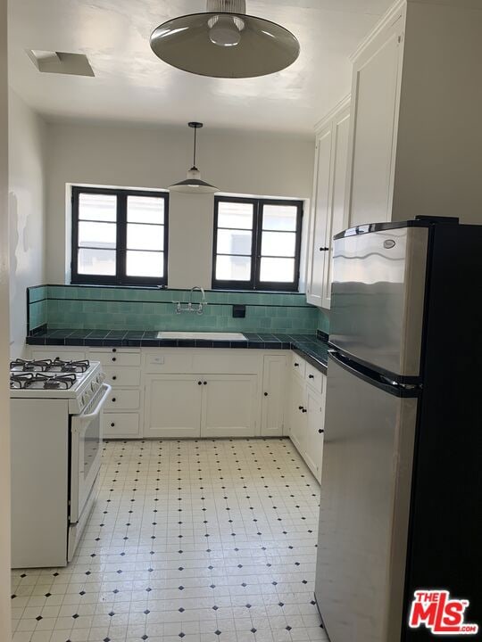 kitchen with stainless steel fridge, white cabinetry, white gas stove, and a healthy amount of sunlight