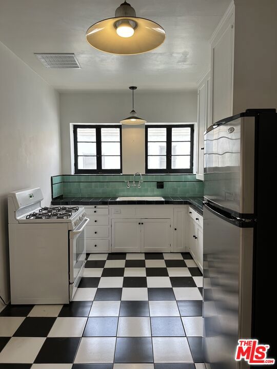 kitchen featuring white cabinets, white range with gas stovetop, sink, and stainless steel refrigerator