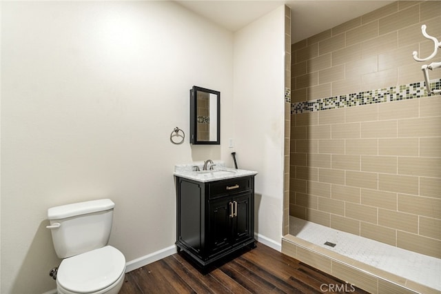 bathroom with a tile shower, hardwood / wood-style floors, vanity, and toilet