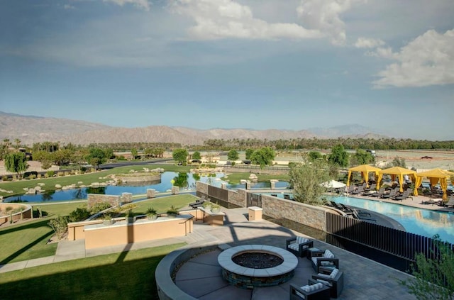 exterior space featuring a water and mountain view, an outdoor fire pit, and a community pool