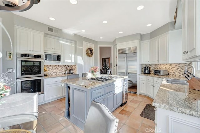 kitchen with a center island, backsplash, sink, built in appliances, and white cabinetry