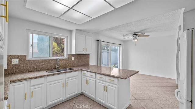 kitchen with kitchen peninsula, sink, tasteful backsplash, white fridge, and white cabinetry