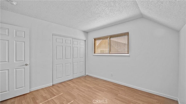 unfurnished bedroom featuring wood-type flooring, a textured ceiling, vaulted ceiling, and a closet