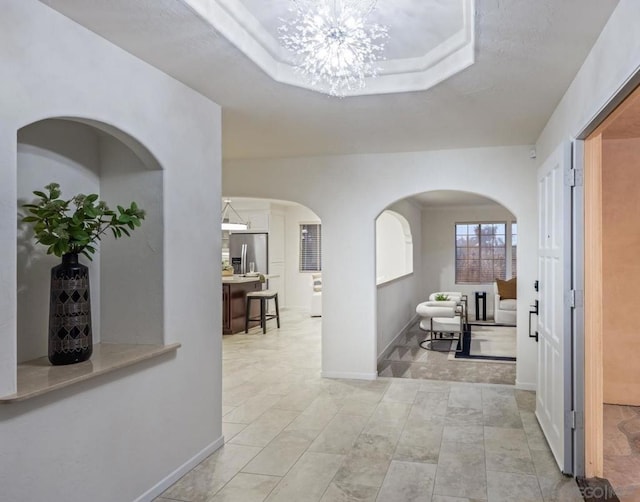 hallway with a raised ceiling and a chandelier