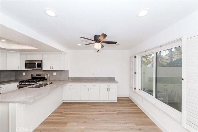 kitchen with white cabinetry, decorative backsplash, kitchen peninsula, stainless steel appliances, and light hardwood / wood-style flooring