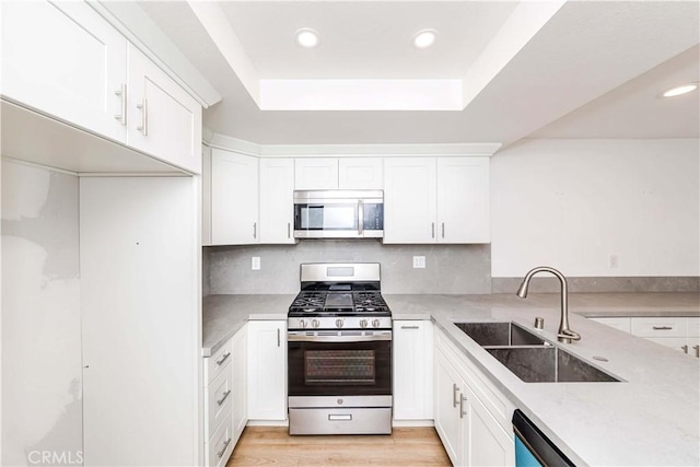 kitchen featuring sink, white cabinetry, light hardwood / wood-style flooring, appliances with stainless steel finishes, and decorative backsplash