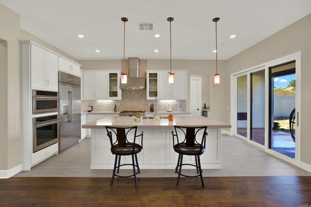 kitchen featuring hanging light fixtures, wall chimney exhaust hood, stainless steel appliances, and a kitchen island