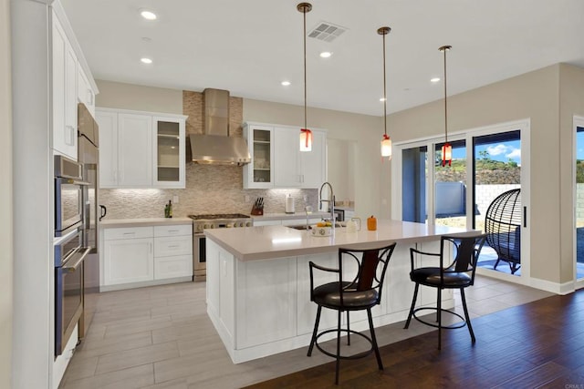 kitchen with sink, wall chimney exhaust hood, a center island with sink, and high end range