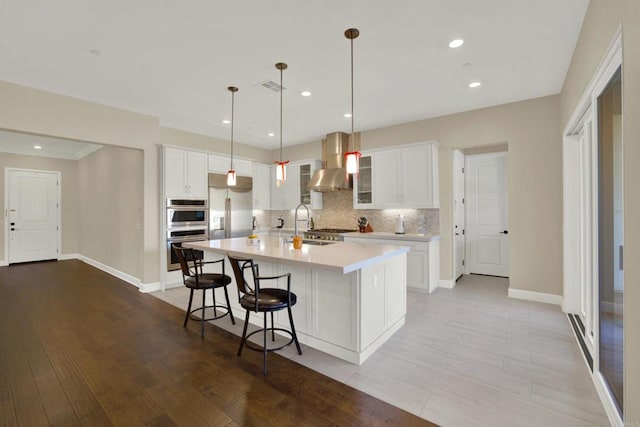 kitchen featuring white cabinetry, wall chimney exhaust hood, a spacious island, and stainless steel appliances