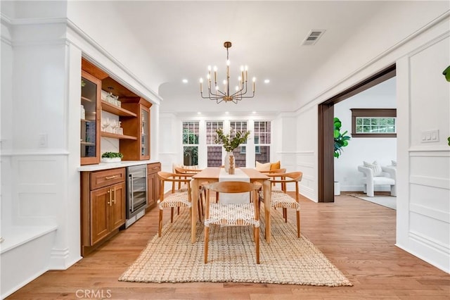 dining room with a chandelier, light wood-type flooring, beverage cooler, and ornamental molding