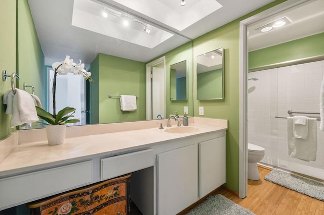 bathroom featuring a skylight, hardwood / wood-style floors, an enclosed shower, toilet, and vanity