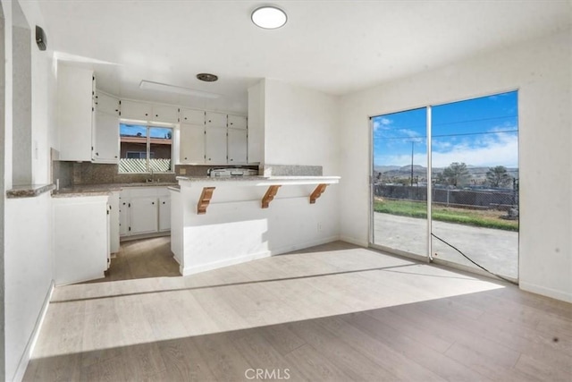 kitchen featuring white cabinets, light wood-type flooring, kitchen peninsula, and a breakfast bar area