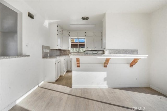 kitchen with kitchen peninsula, backsplash, hardwood / wood-style flooring, white cabinetry, and a breakfast bar area