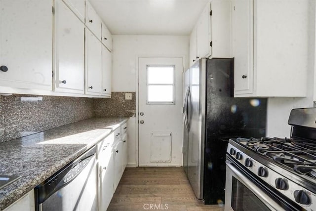 kitchen featuring tasteful backsplash, dark stone counters, stainless steel appliances, wood-type flooring, and white cabinetry