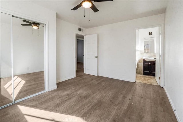 unfurnished bedroom with ceiling fan, ensuite bath, wood-type flooring, and a closet