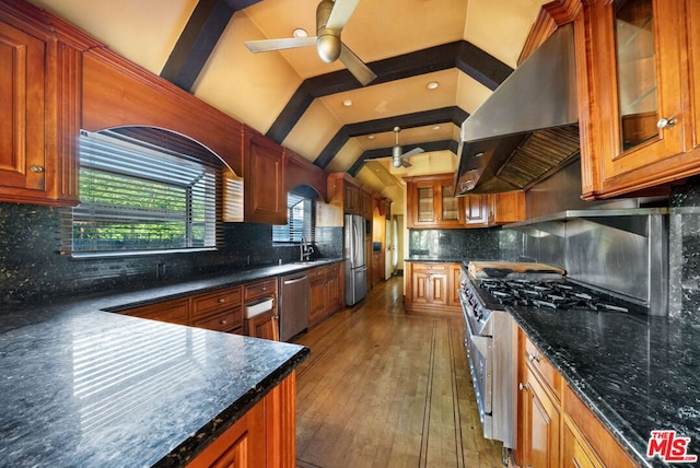 kitchen featuring wall chimney exhaust hood, decorative backsplash, vaulted ceiling with beams, and stainless steel appliances