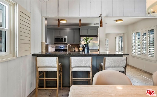 kitchen featuring appliances with stainless steel finishes, a kitchen breakfast bar, tasteful backsplash, wooden walls, and hanging light fixtures