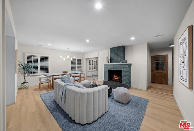 living room with an inviting chandelier, light hardwood / wood-style floors, and a brick fireplace