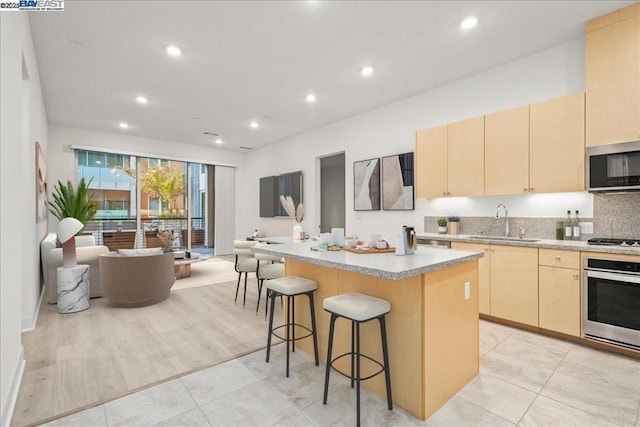 kitchen with a kitchen island, a kitchen bar, light brown cabinets, stainless steel appliances, and sink