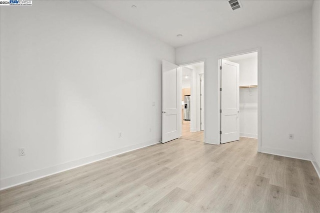 unfurnished bedroom featuring stainless steel refrigerator with ice dispenser, a closet, a walk in closet, and light hardwood / wood-style flooring