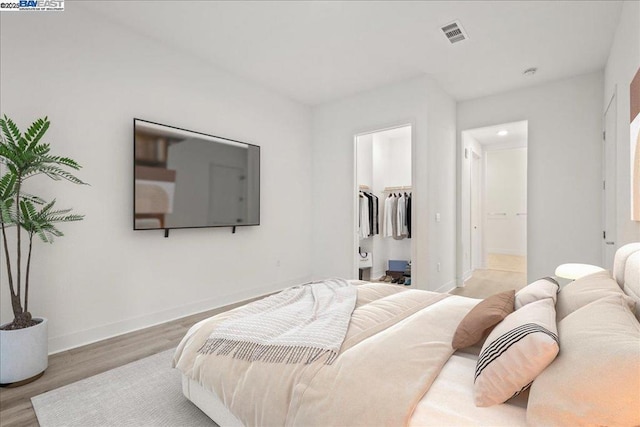 bedroom with a closet, a walk in closet, connected bathroom, and wood-type flooring