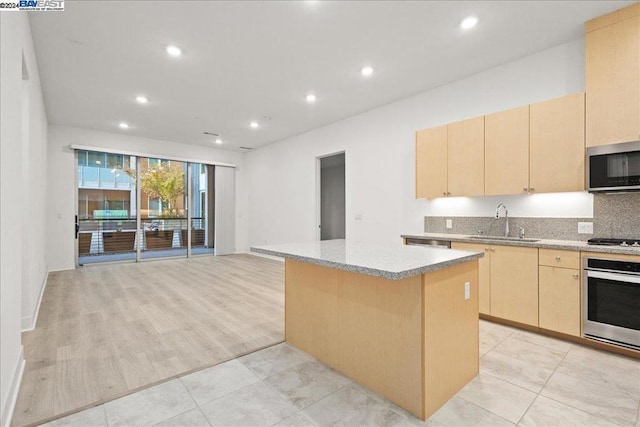 kitchen with appliances with stainless steel finishes, backsplash, light brown cabinets, a center island, and sink