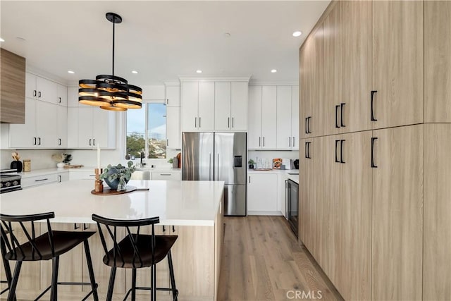 kitchen with decorative light fixtures, stainless steel fridge, light wood-type flooring, and white cabinetry