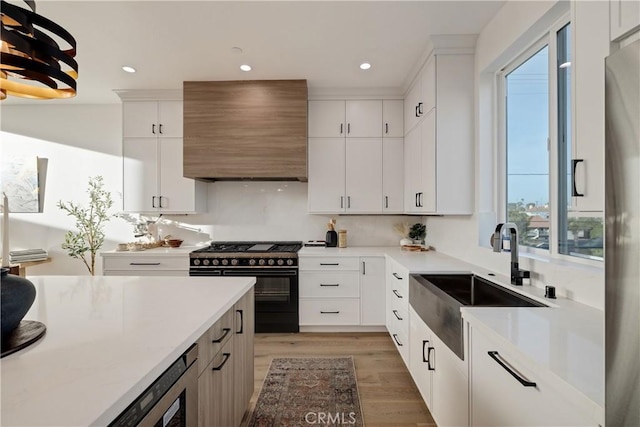 kitchen with white cabinetry, sink, high end black range, custom range hood, and light wood-type flooring