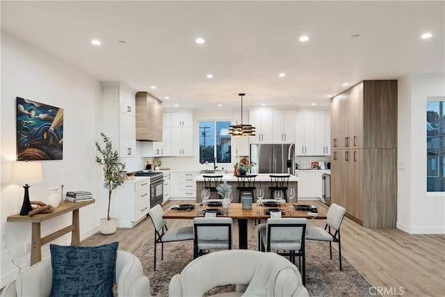 kitchen featuring wall chimney range hood, light hardwood / wood-style flooring, decorative light fixtures, white cabinets, and appliances with stainless steel finishes