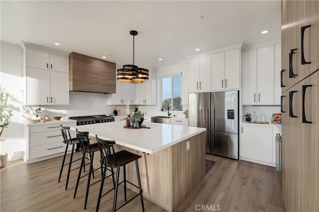 kitchen featuring custom range hood, stainless steel appliances, light hardwood / wood-style flooring, white cabinets, and hanging light fixtures