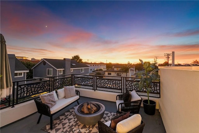 patio terrace at dusk featuring a balcony and an outdoor living space with a fire pit