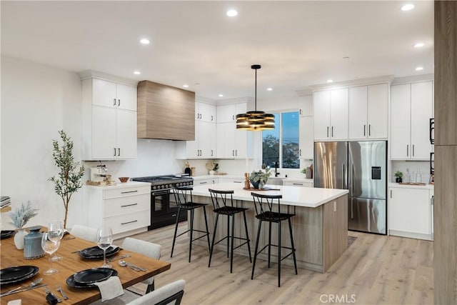 kitchen with pendant lighting, high end range, white cabinets, wall chimney exhaust hood, and stainless steel fridge