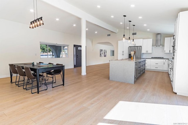 kitchen with stainless steel fridge with ice dispenser, wall chimney exhaust hood, a kitchen island, white cabinets, and decorative light fixtures